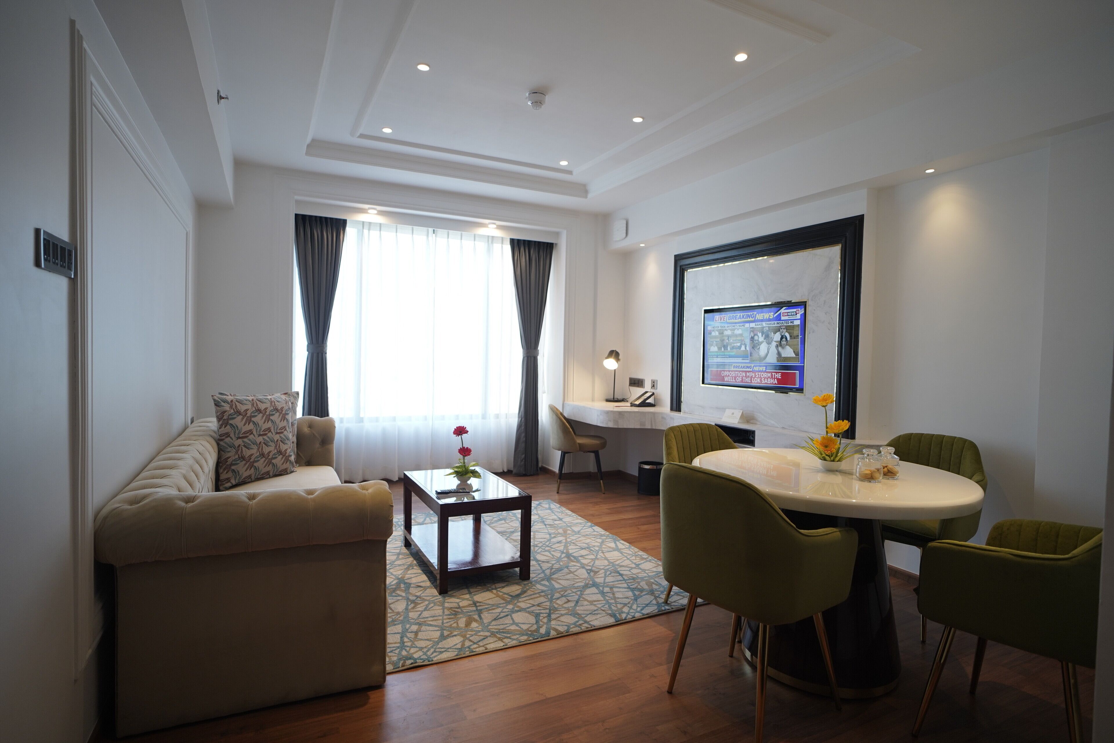 A modern living room with a sofa, a coffee table, a dining table with chairs, and a large window with curtains.