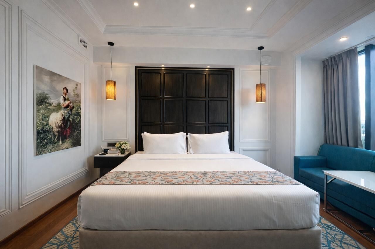 A hotel room with a large bed, two bedside tables, a nightstand, a blue sofa, and a painting on the wall.