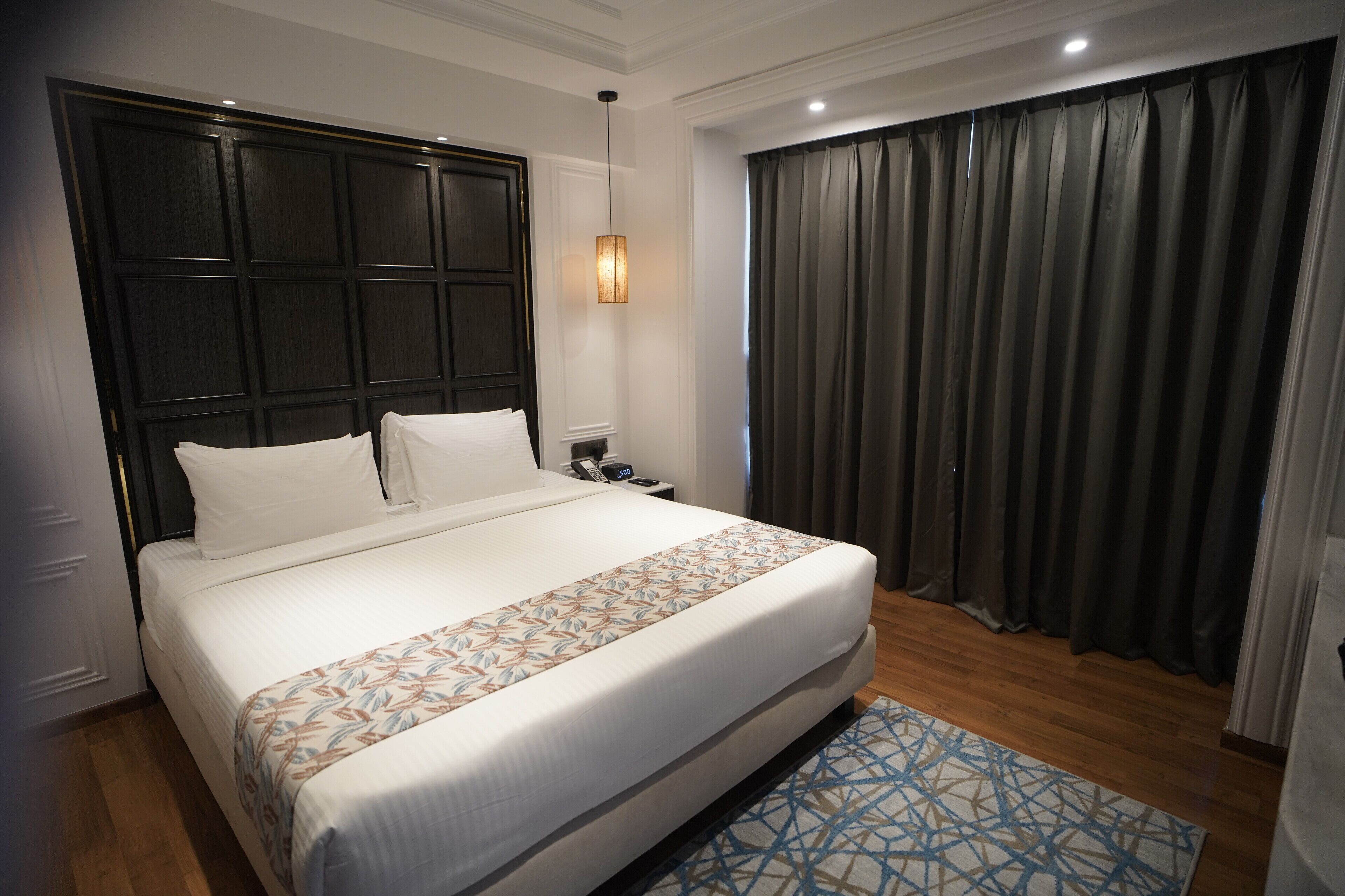 Uma cama bem arrumada com colcha estampada, cabeceira escura e mesa de cabeceira com abajur.