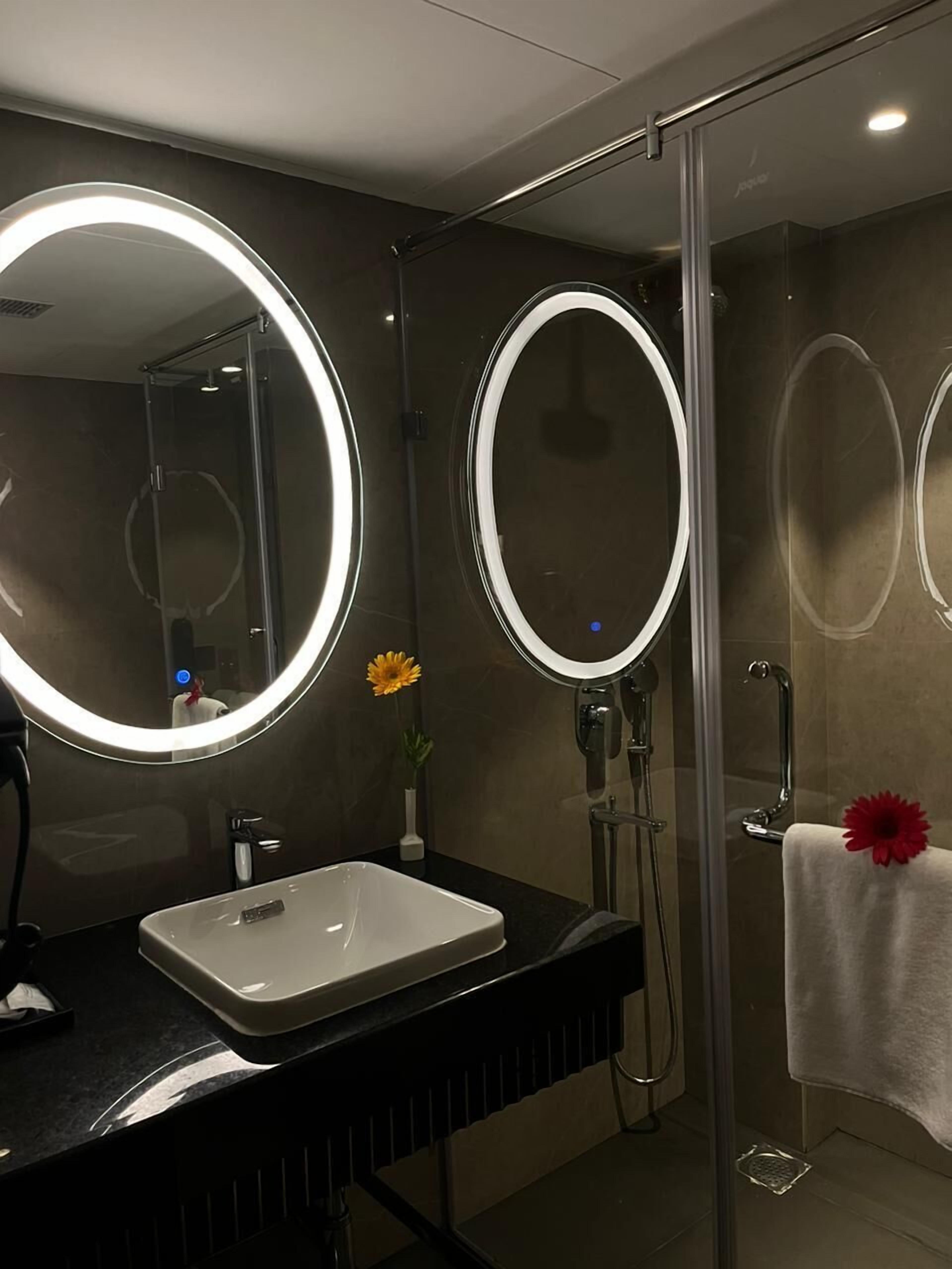 A modern bathroom with a glass-enclosed shower, a white sink, and two round mirrors with built-in lighting.