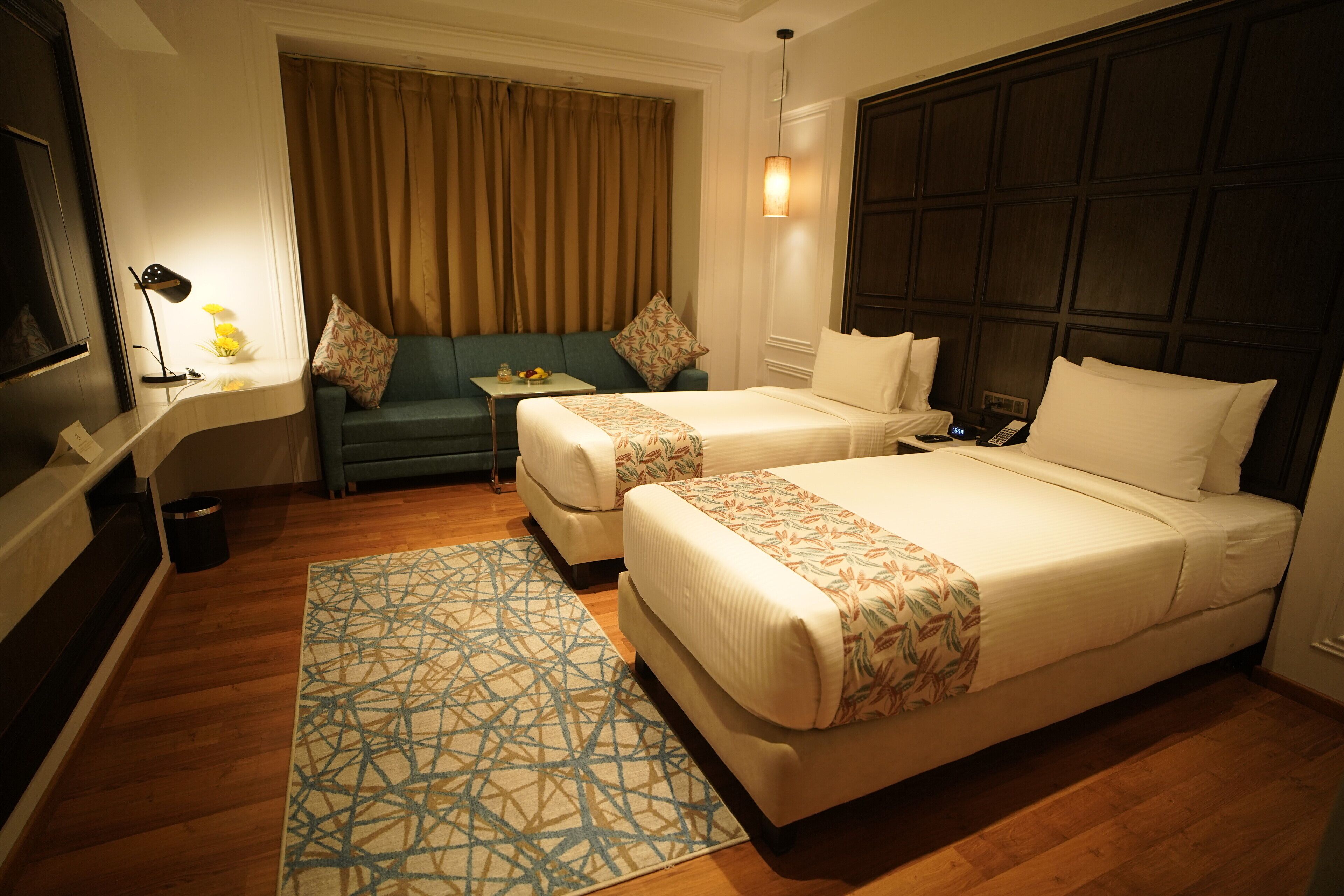 A hotel room with two beds, a sofa, a small table, and a TV.