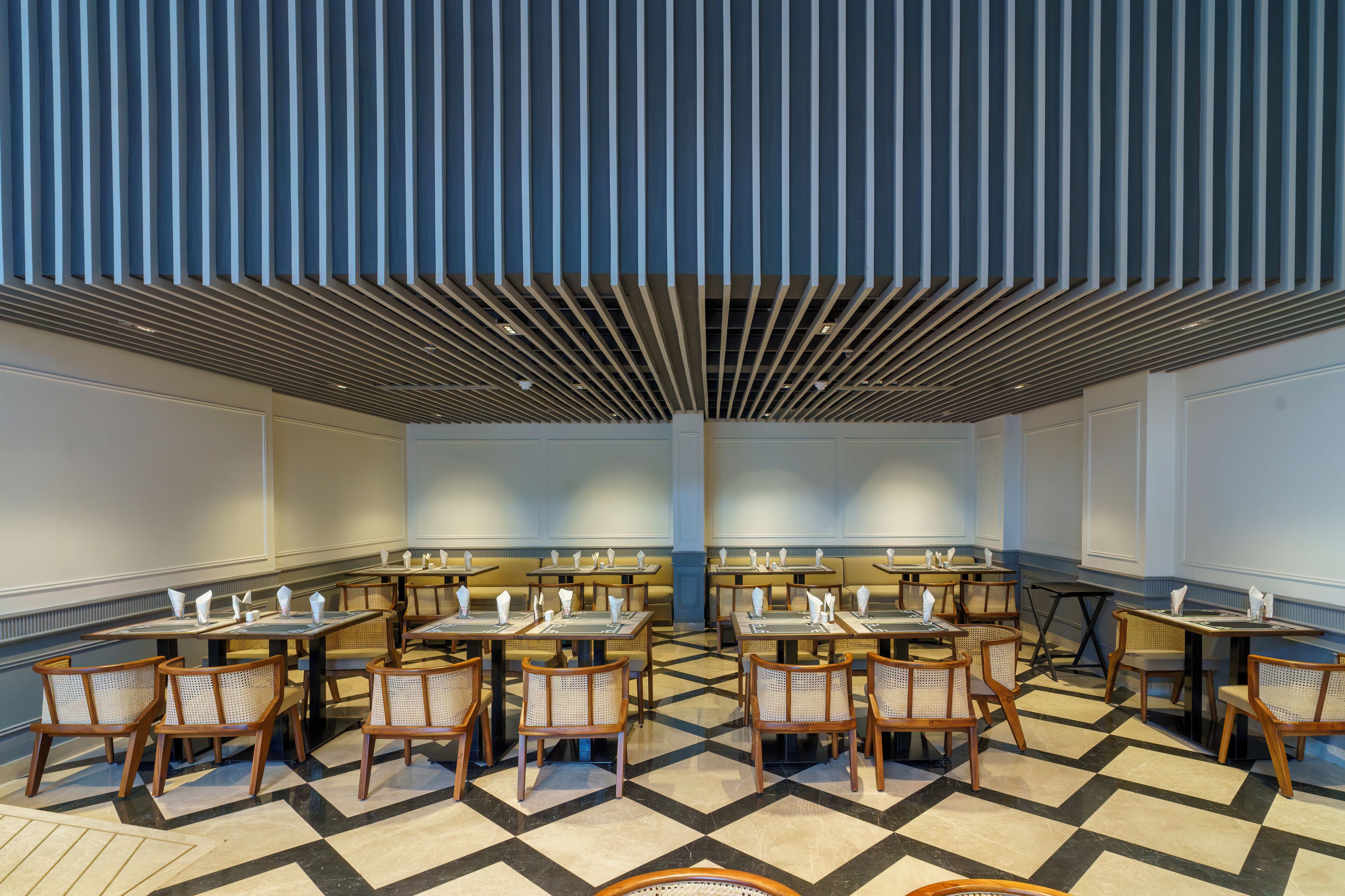 A restaurant with a checkered floor, wooden chairs, and tables set with white napkins and plates.