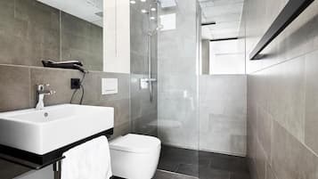 Un baño moderno con un lavamanos grande de color blanco, un inodoro y una zona de ducha con mampara de vidrio.
