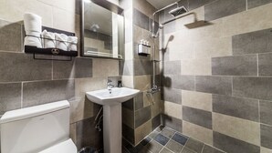 A modern bathroom with a white toilet, a sink, a shower with a handheld showerhead, and a towel rack with neatly folded towels. - Design Hotel Khan (Suwon)