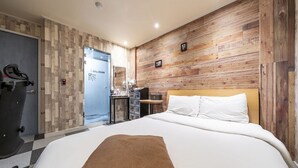 A hotel room with a large bed, a wooden wall panel, a desk with a chair, and a bike storage area. - Design Hotel Khan (Suwon)