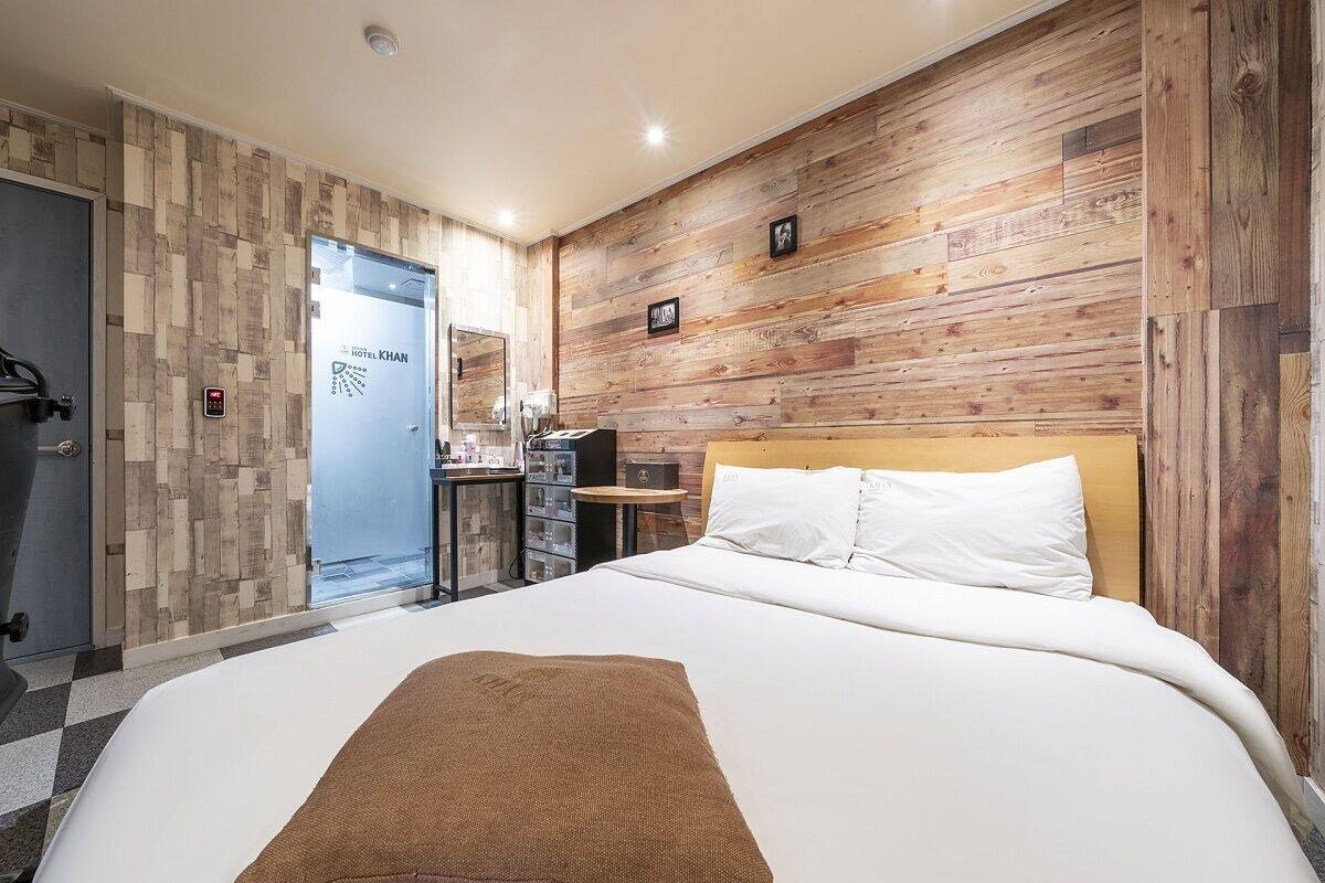 A hotel room with a large bed, a wooden wall panel, a desk with a chair, and a bike storage area.
