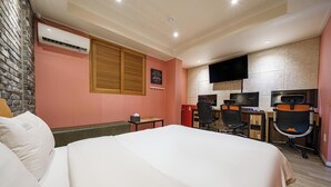A hotel room with a bed, a desk, two chairs, a television, and an air conditioning unit. - Design Hotel Khan (Suwon)