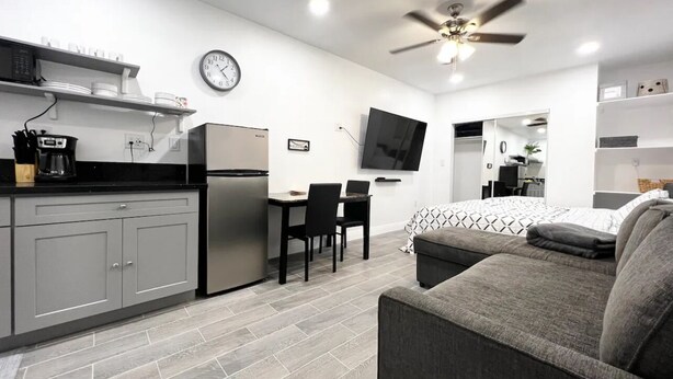 A modern kitchen with grey cabinets, a built-in oven, and a dining area with a table and chairs. - Cozy Private Studio (Quartz Hill)
