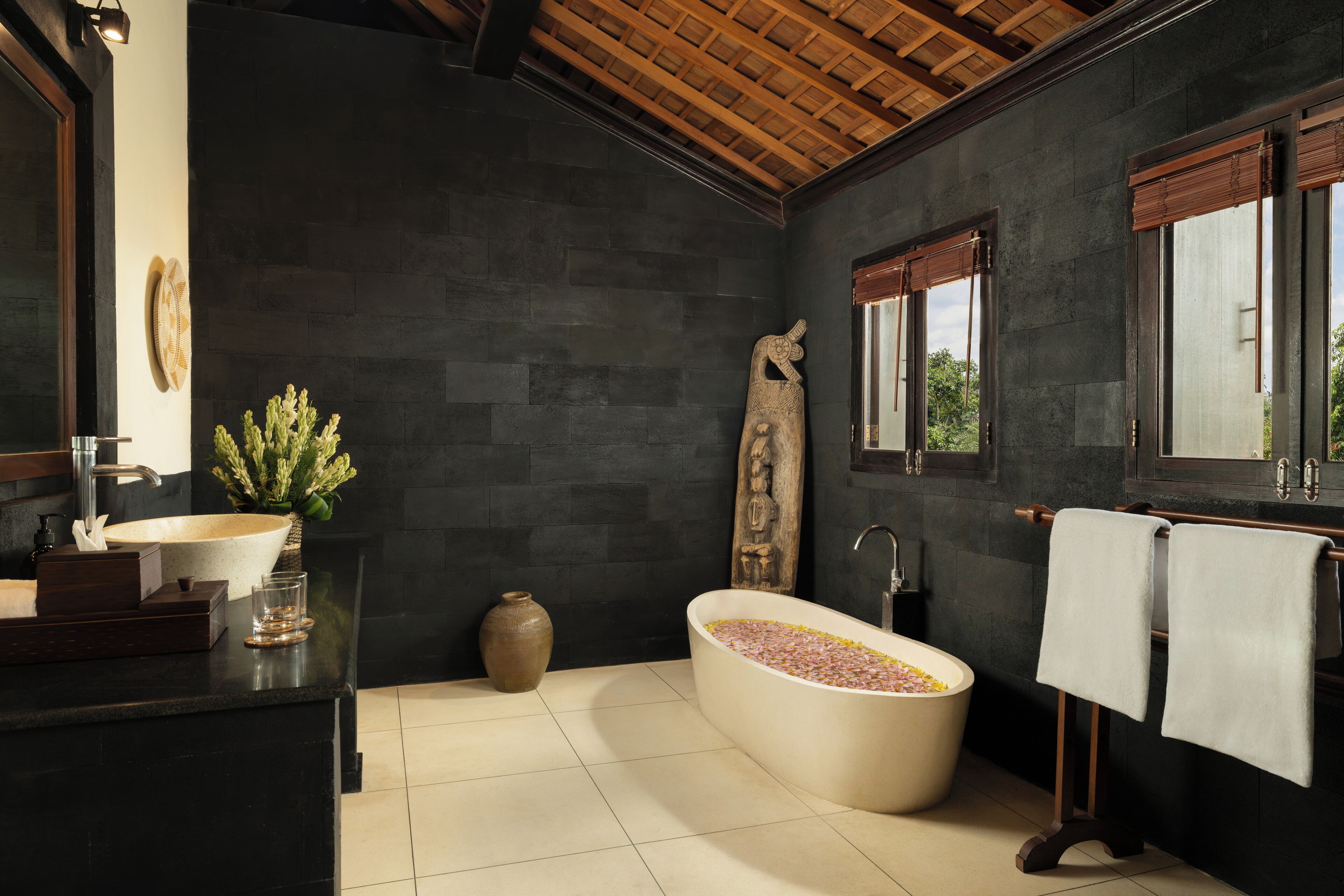 Ein modernes Badezimmer mit einer freistehenden Badewanne, einem großen Spiegel und einer Holzbalkendecke.