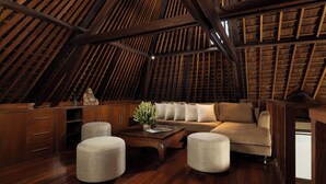 Una habitación acogedora en el ático con techo inclinado de madera, un sofá, otomanas, una mesita de centro y armarios empotrados de madera.