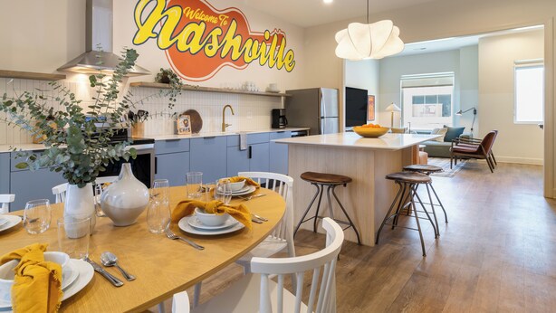A modern kitchen with a central island, white cabinetry, and a dining area with a yellow tablecloth.