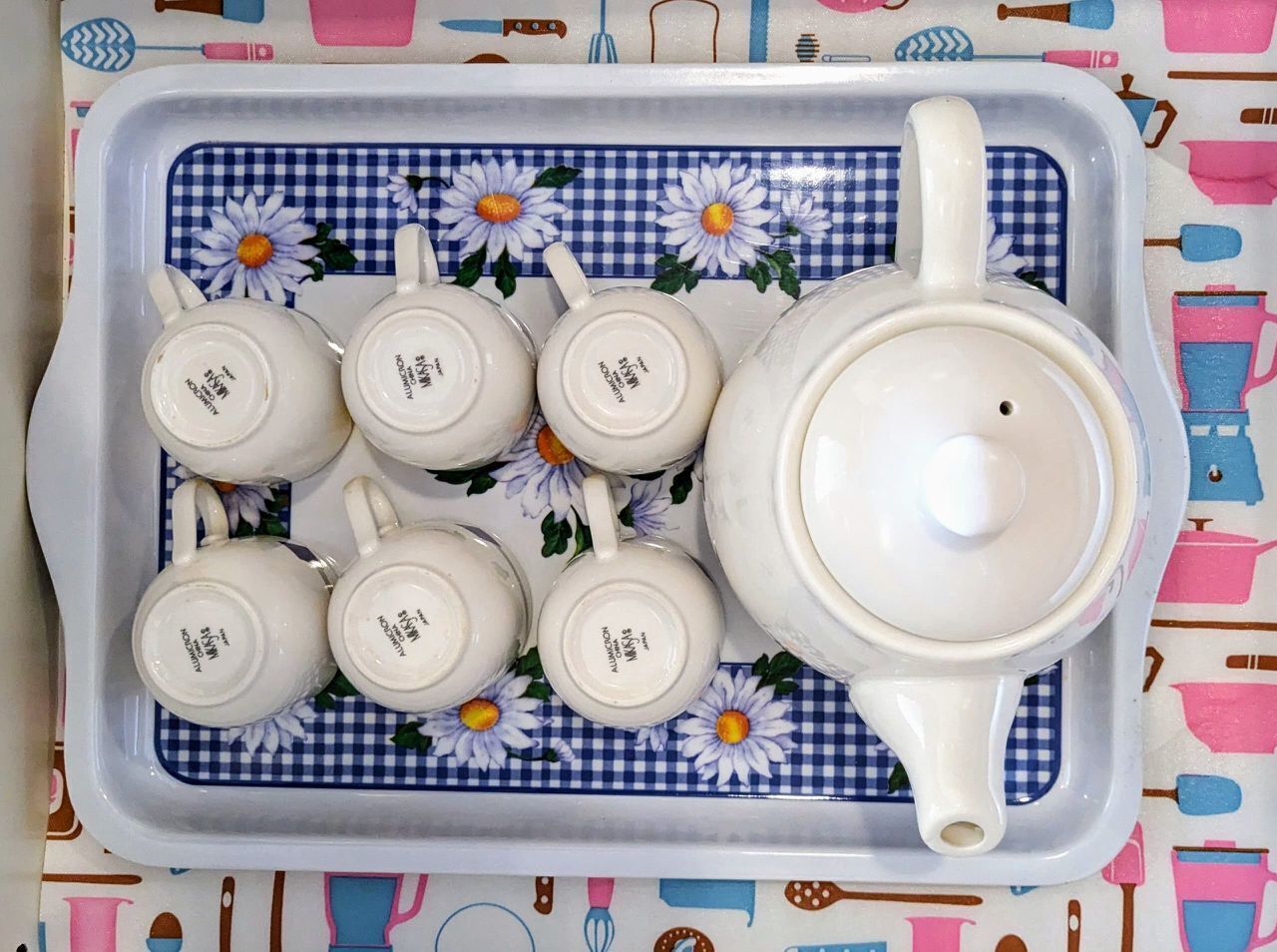 A tray with teapots and cups on a checkered cloth with floral patterns.