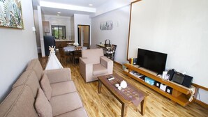 Una sala de estar con sofá, sillón, mesa de centro, televisor y mueble de televisión de madera.