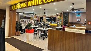 Interior de una cafetería con mesas, sillas y ventiladores de techo.