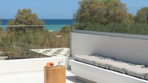 A modern balcony with a view of the sea, a wooden side table with fruit and a glass, and a white cushioned bench. - Costa Villa , Walk to Sandy Beach & Heated Pool (88XM+XWC Pirgos)