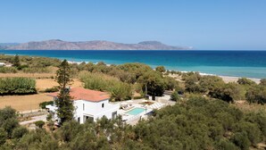 A coastal property with a swimming pool, white building, and views of the sea and mountains. - Costa Villa , Walk to Sandy Beach & Heated Pool (88XM+XWC Pirgos)
