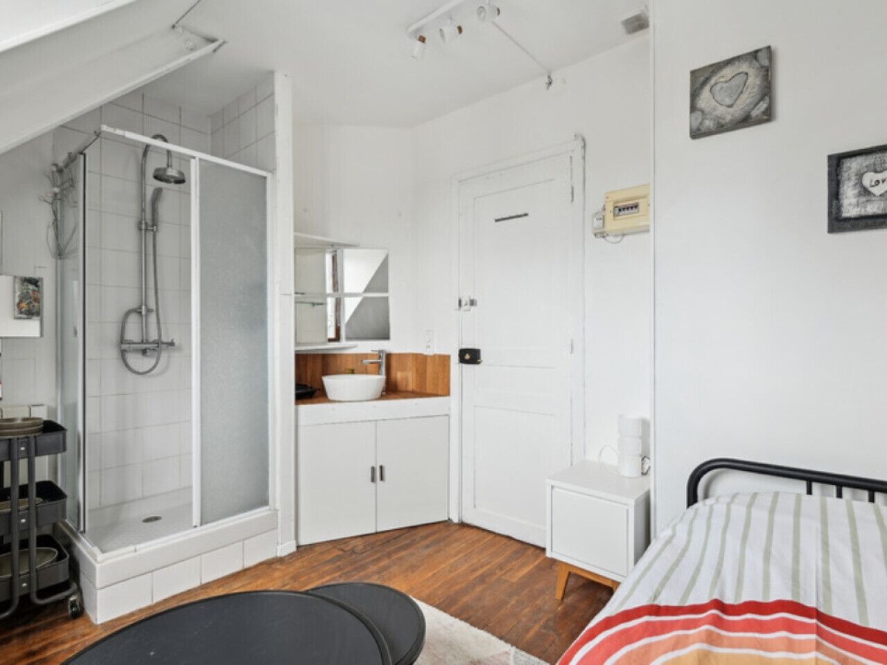 Een kamer met een douche, wastafel, bed en een klein tafeltje.