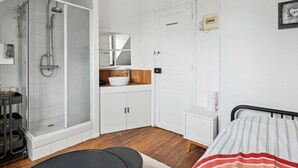A room with a shower, a sink, a bed, and a small table. - 1. Studio Porte Dauphine Paris 16ème (Paris)