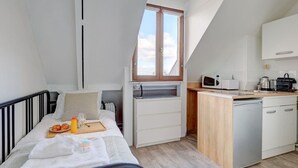 A compact room with a bed, a small kitchenette, a window, and a view of the sky. - Studio Porte Dauphine Paris 16ème (Paris)