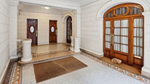A grand hallway with a marble floor, a large wooden door with glass panels, and a dog resting near the door. - Studio Porte Dauphine Paris 16ème (Paris)