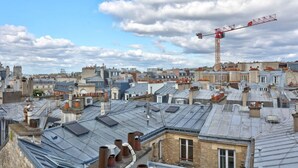 A cityscape with multiple rooftops, a construction crane, and a partly cloudy sky. - Studio Porte Dauphine Paris 16ème (Paris)