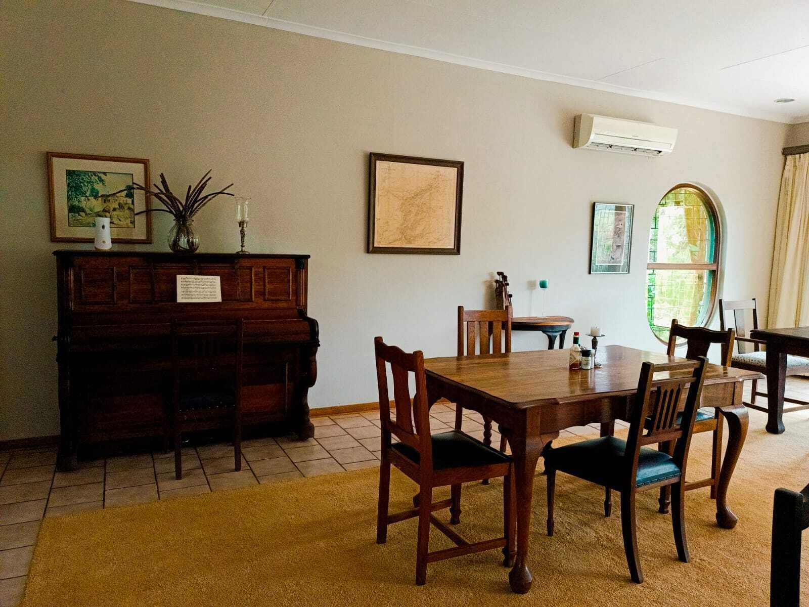 A dining area with a wooden table and chairs, a piano, and framed artwork on the walls.