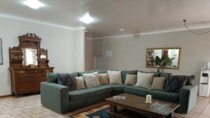 A living room with a sectional sofa, a wooden cabinet, a coffee table, and a large mirror. - Pecan Farm Guesthouse (Louis Trichardt)