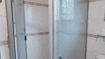 A bathroom with a glass-enclosed shower, a toilet, and a toilet paper holder.