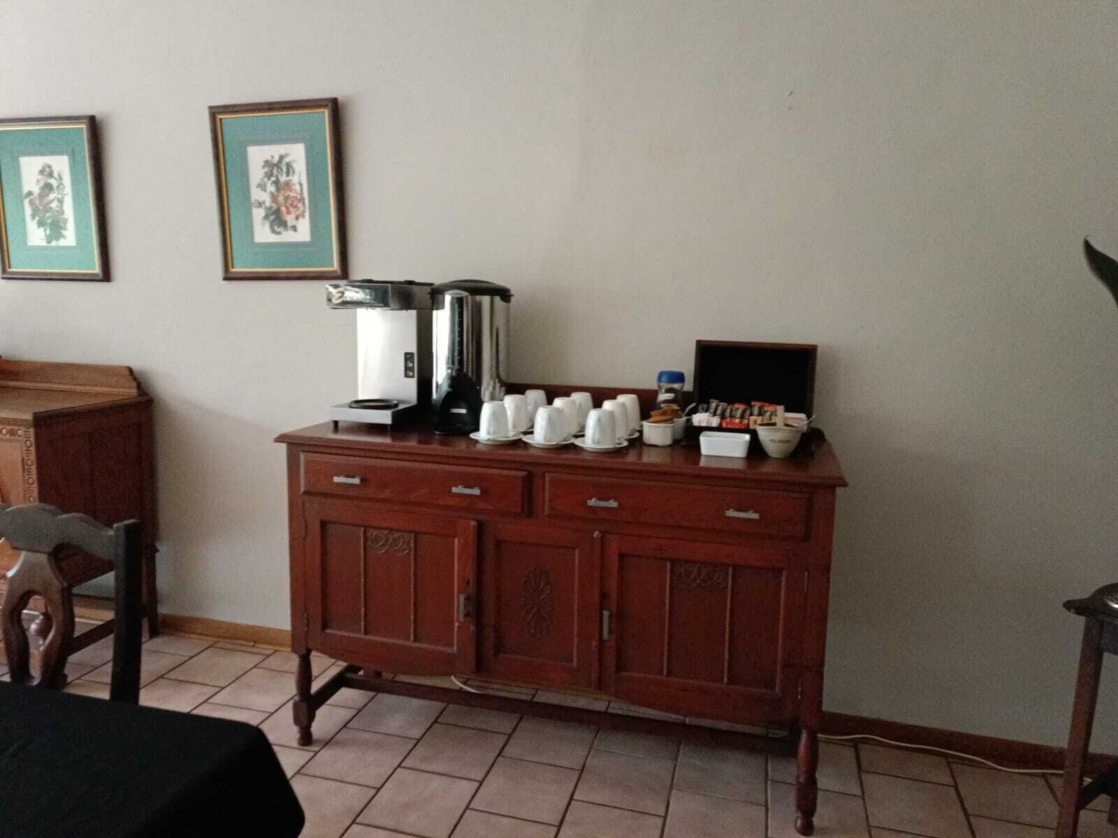 Una habitación de hotel con un mueble de madera que contiene una cafetera, tazas y un bol de aperitivos.