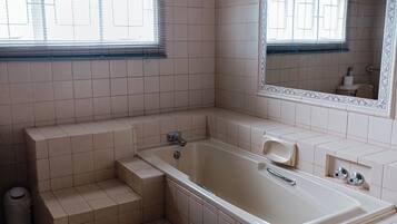 A bathroom with a bathtub, a window, and a mirror.
