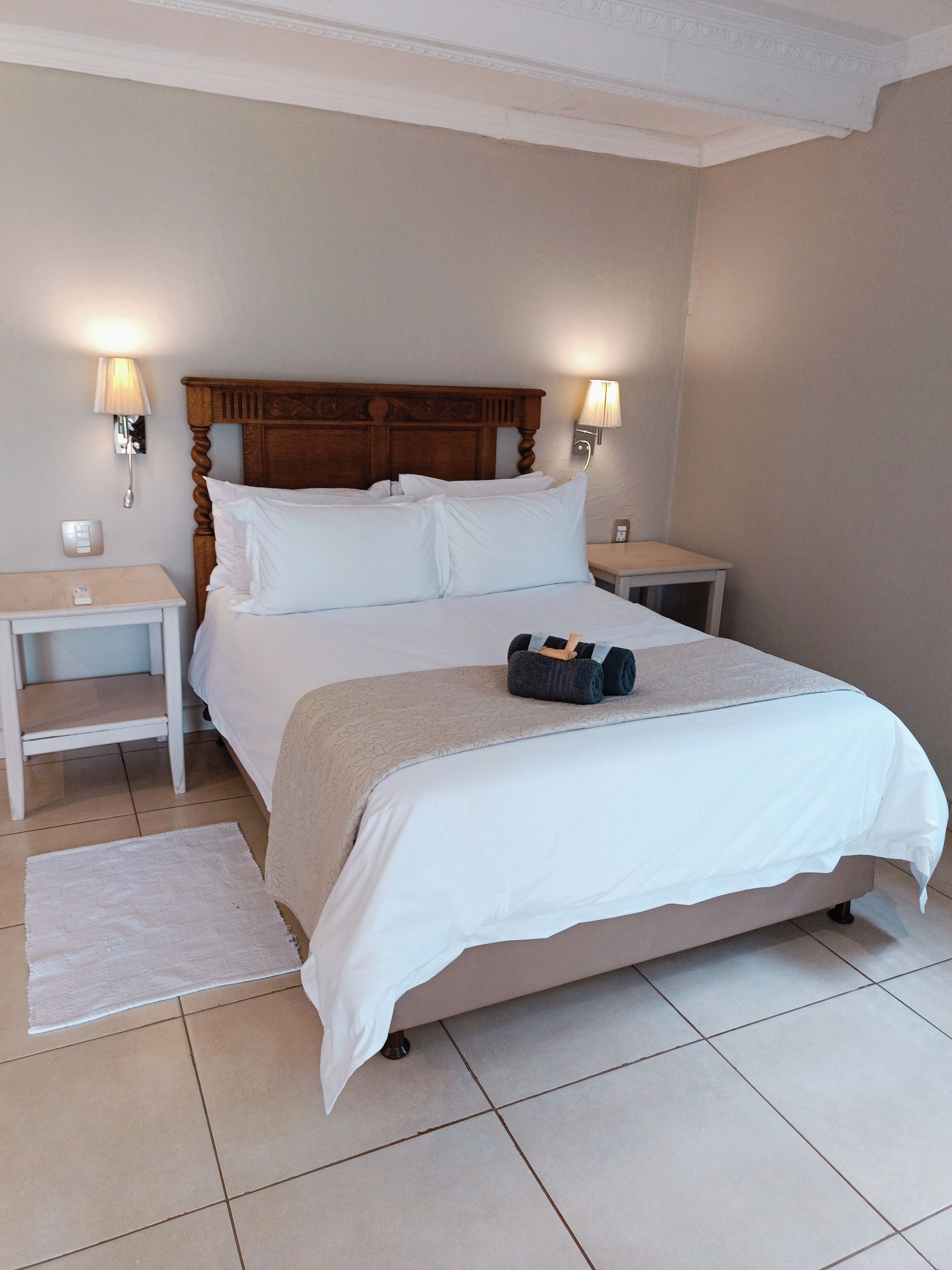 A neatly made bed with a wooden headboard, two bedside tables with lamps, and a small rug on the floor.