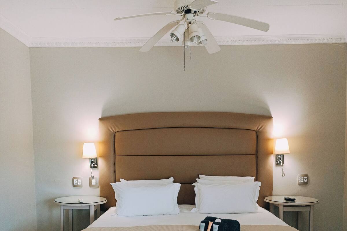 Een hotelkamer met een groot bed, twee nachtkastjes met lampen, een plafondventilator en een kamerkleed met dessin.