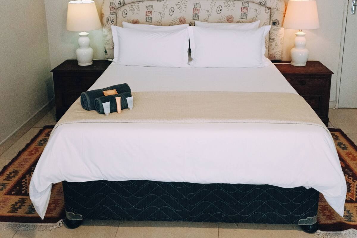 Een net opgemaakt bed met witte lakens, twee nachtkastjes met lampen, en een bed hoofddeksel met patroon.
