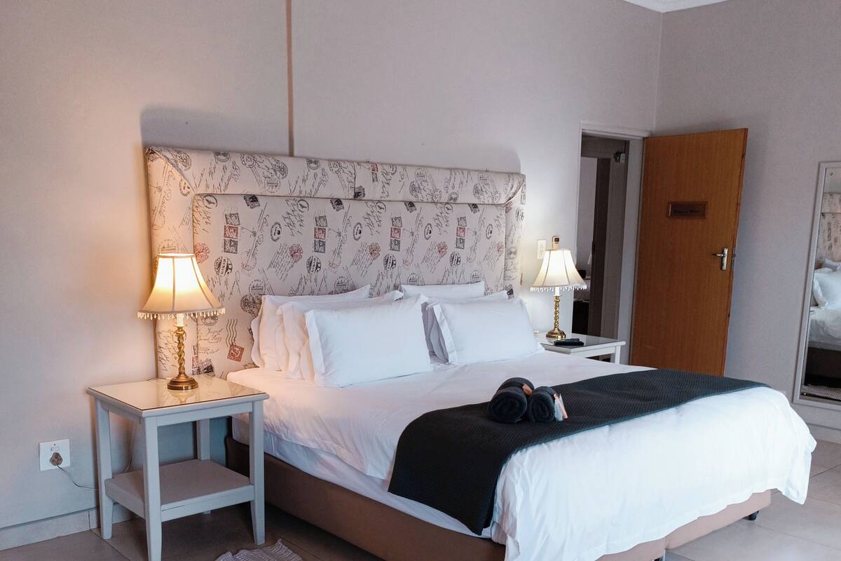 Een netjes opgemaakt bed met witte lakens en een zwart deken, een nachtkastje met een lamp, en een gestreept hoofdbord.