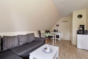 A compact living space with a sofa, a small table, a kitchenette, and a dining area.