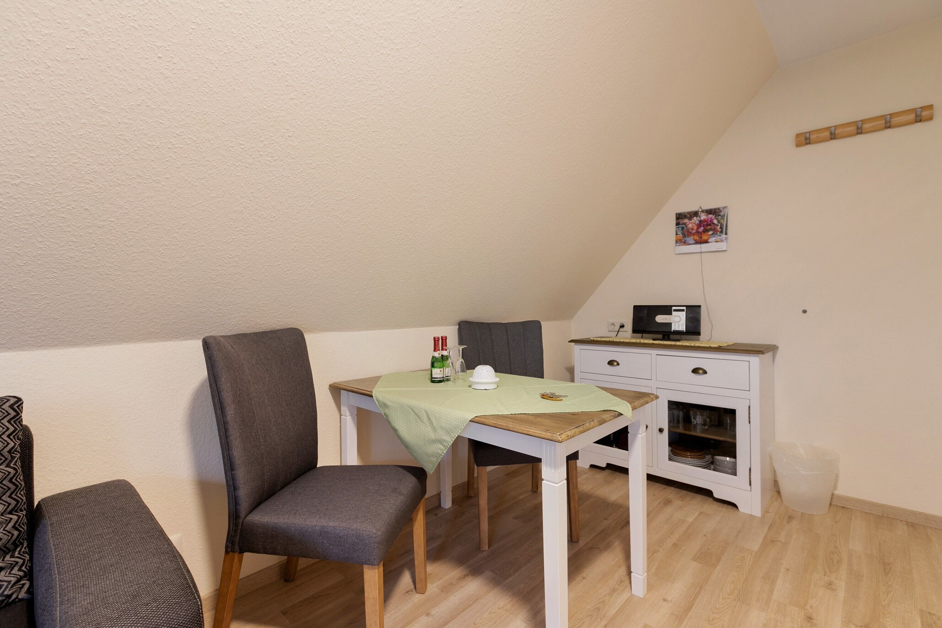 A small, cozy room with a dining table, a chair, a cabinet, and a wall-mounted picture.