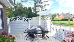 Un patio con una mesa, sillas, una valla blanca y vistas a una calle residencial.