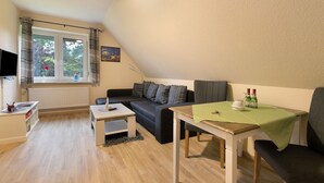 Un acogedor loft con sofá, una mesita, televisor y ventana con cortinas.