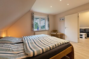 A bedroom with a bed, a window, a chair, and a door.
