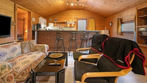 A cozy cabin interior with a wooden ceiling, a sofa, a dining table, and a kitchen area. - 'Holzhaus Grimm' with private terrace and Wi-Fi (Fedderingen)