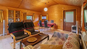 A wooden cabin interior with a dining area, two chairs, a sofa, and a television. - 'Holzhaus Grimm' with private terrace and Wi-Fi (Fedderingen)