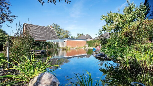 A tranquil pond with surrounding greenery and a brick building in the background. - 'Holzhaus Grimm' with private terrace and Wi-Fi (Fedderingen)