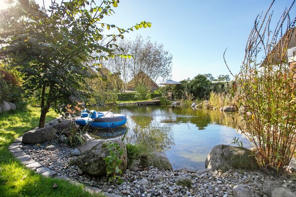 A serene garden with a pond, a small boat, and a house in the background.