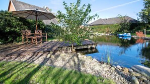 A wooden deck with a table and chairs, a small tree, and a pond with a boat. - 'Holzhaus Grimm' with private terrace and Wi-Fi (Fedderingen)