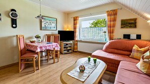 Een gezellige woonkamer met een eettafel, stoelen, een bank, een televisie en een raam met gordijnen.