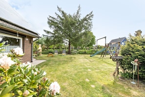 A residential backyard with a grassy lawn, a large tree, a swing set, and a playhouse. - Apartment 'Ferienwohnung Sven' with Shared Garden and Wi-Fi (Langenhorn)