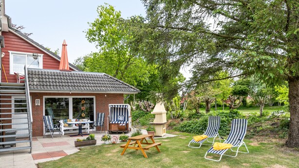 Een achtertuin met terras, een tafel, stoelen, een klein speelhuisje en twee loungesteilen.