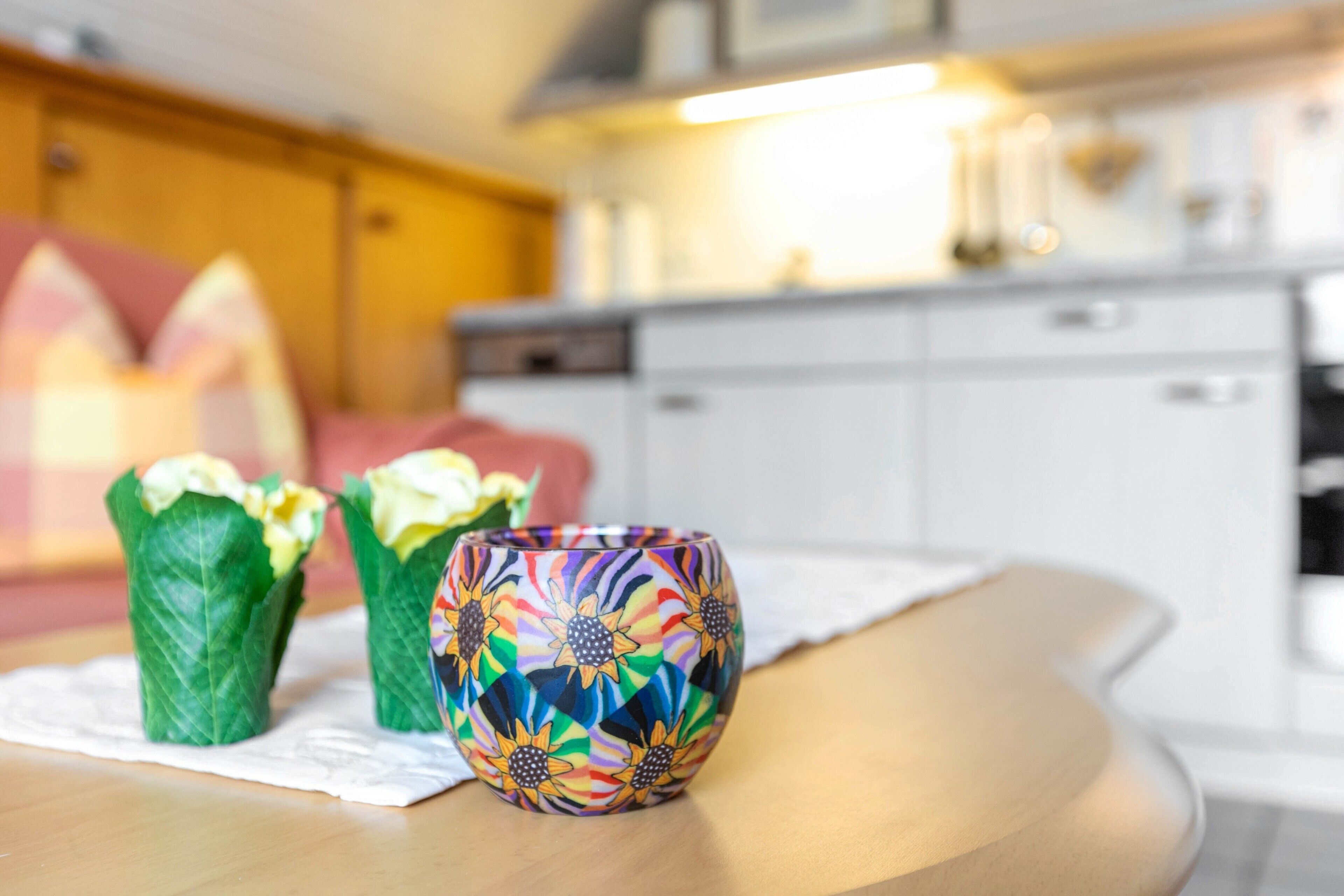 Ein Tisch mit einer bunten Vase und zwei verpackten Gegenständen, eine Küche im Hintergrund.