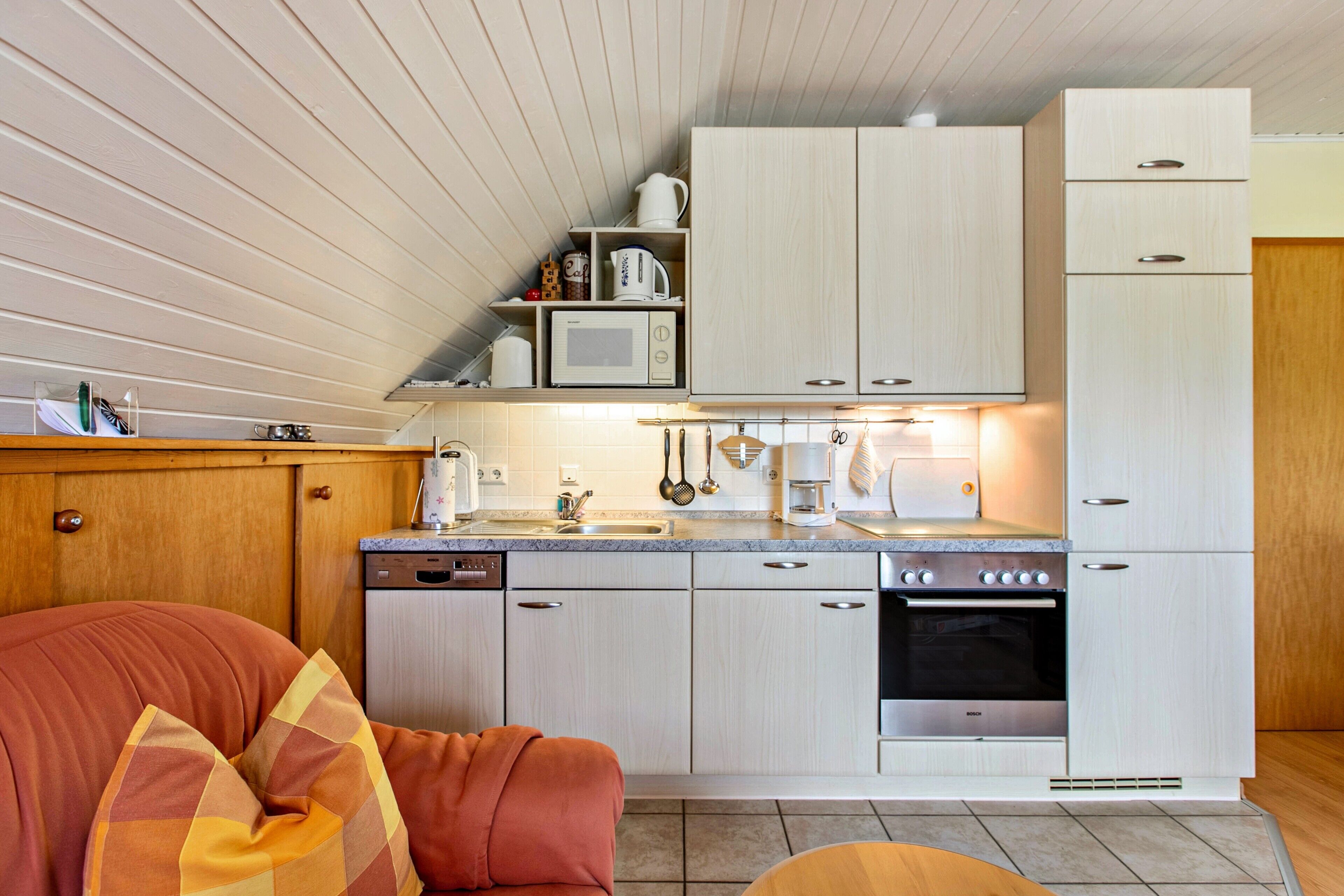 Una cocina compacta con armarios blancos, microondas, cafetera y lavavajillas.