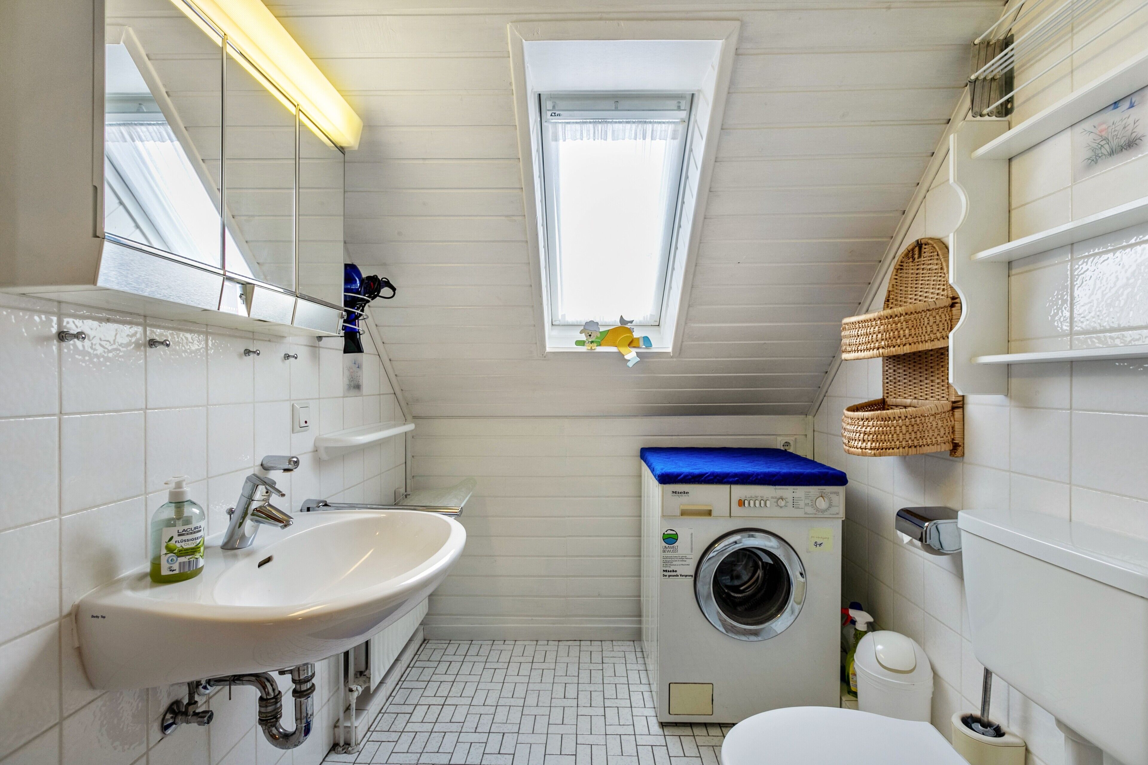 A compact bathroom with a sink, mirror, window, and washing machine.